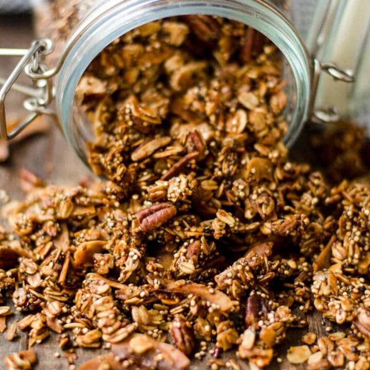 Homemade granola with nuts spilling out of a clear storage jar.