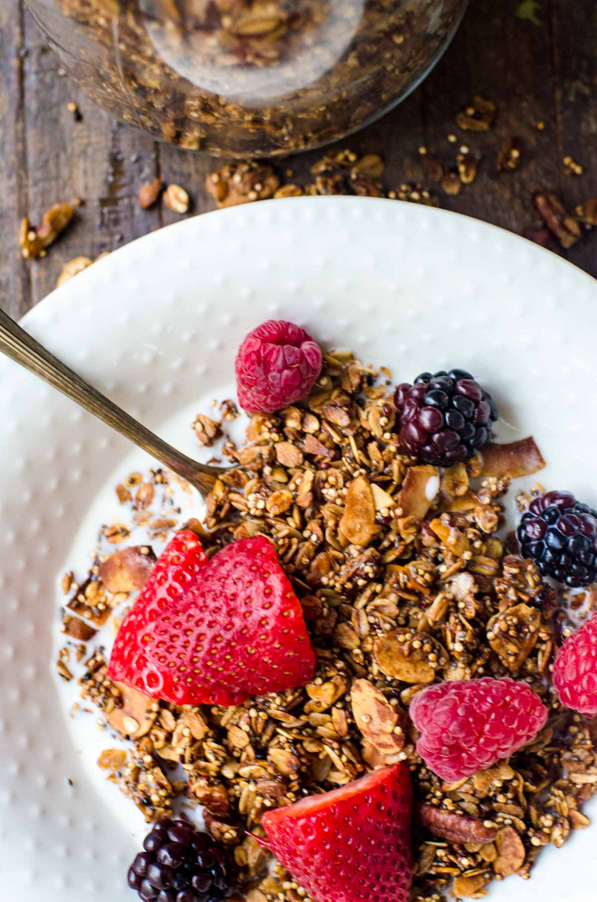 Granola and fresh berries in a white bowl with milk.