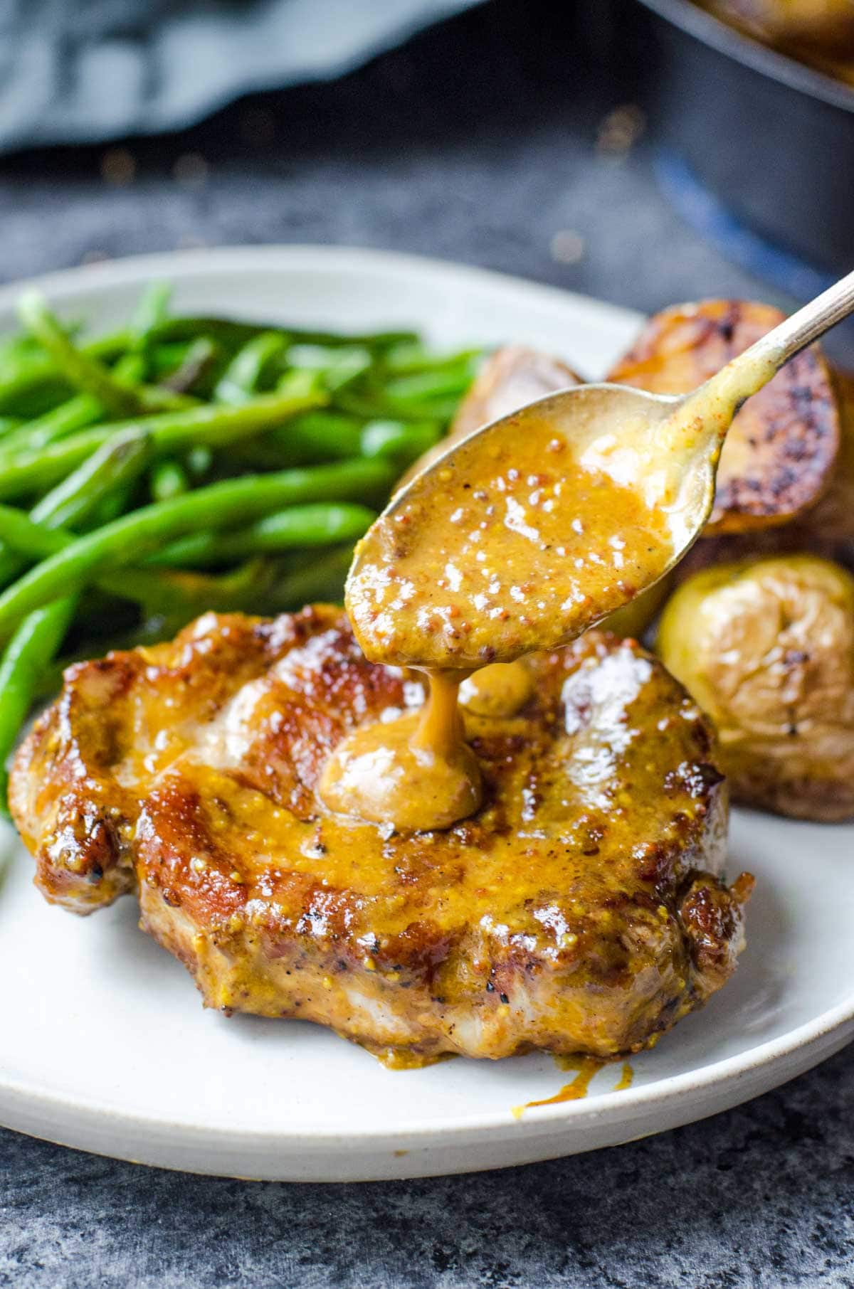 A spoon drizzling honey mustard on pork chop.