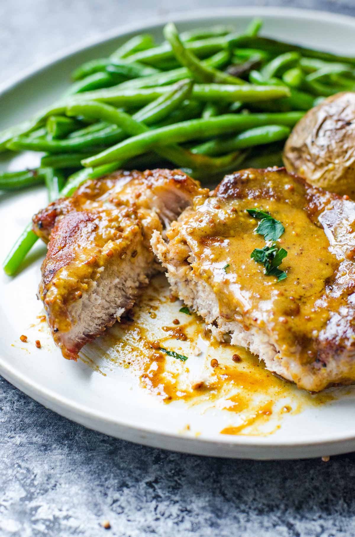 A plate of green beans and cut pork chop with honey mustard.