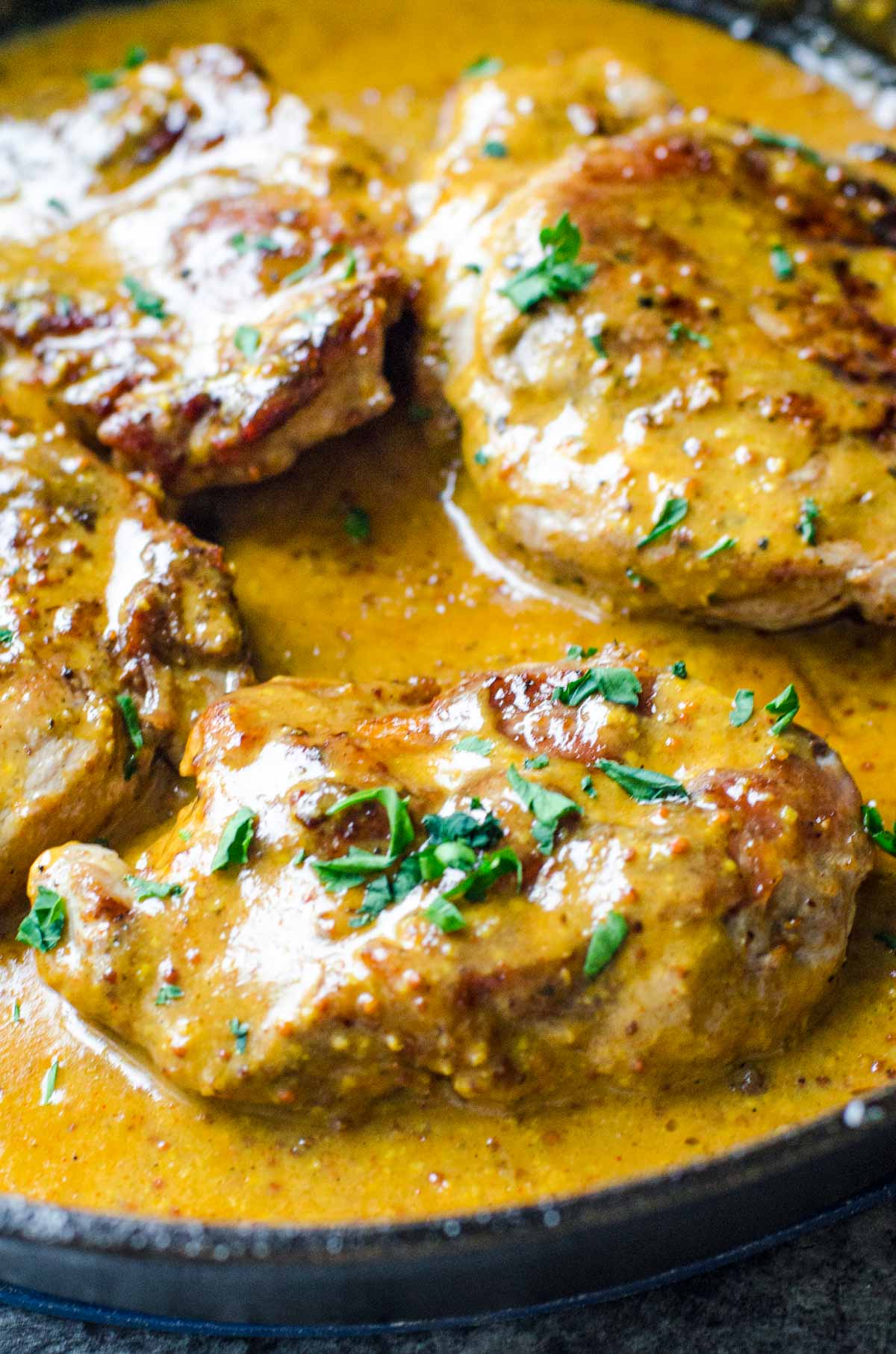 Pan fried pork chops simmering in honey mustard sauce.