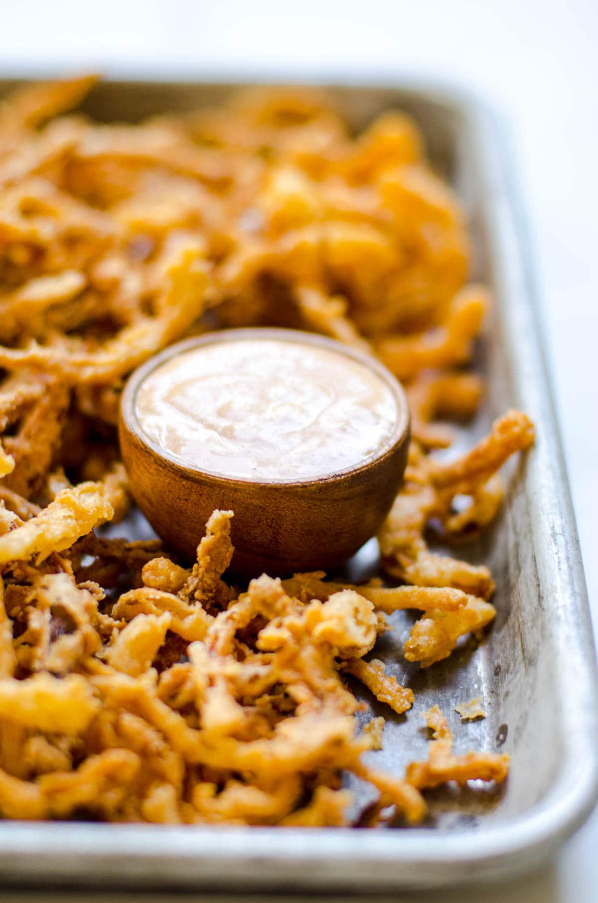 A bowl of sauce on a pan of fried onion strings.