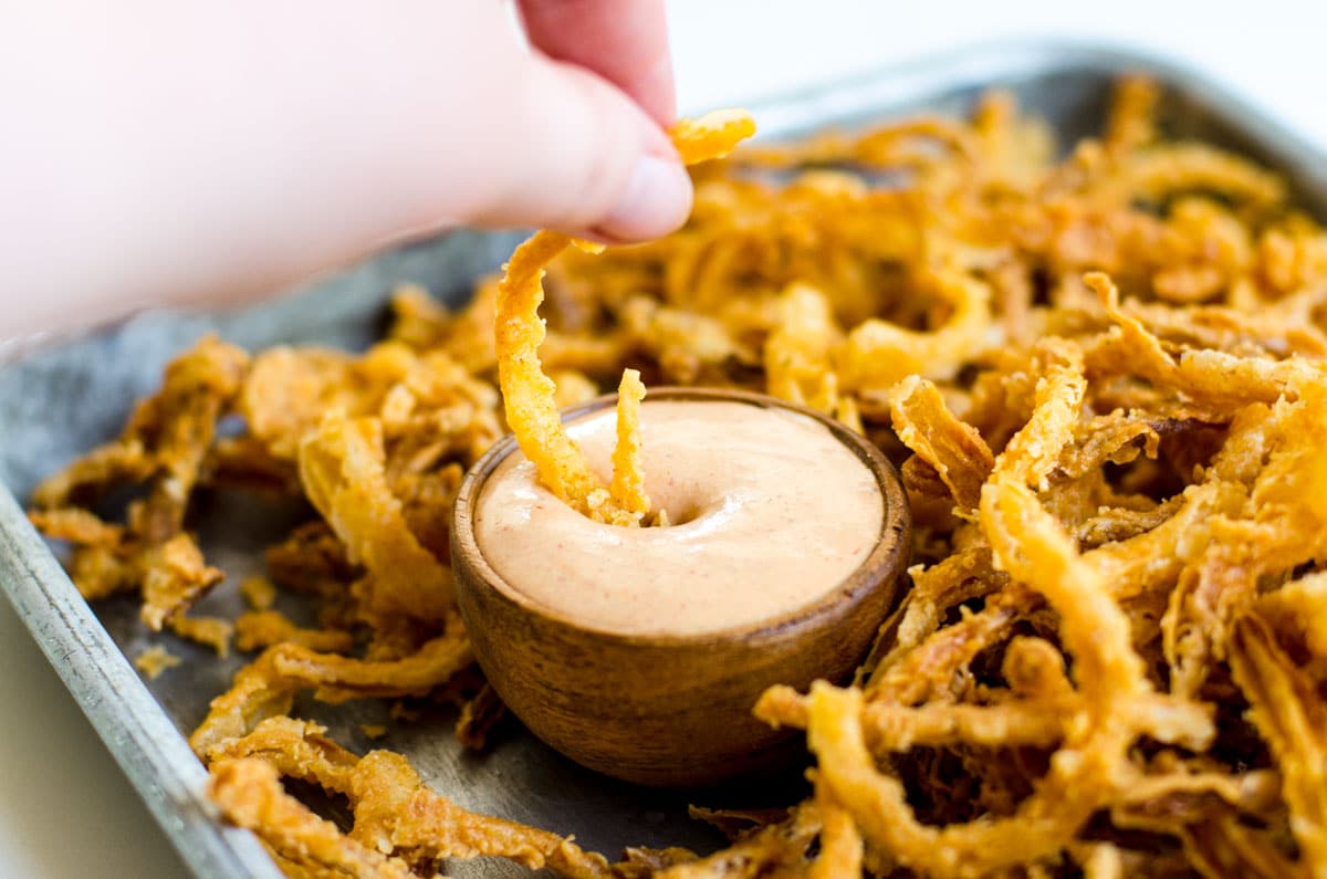 A hand dipping onion strings in sauce.