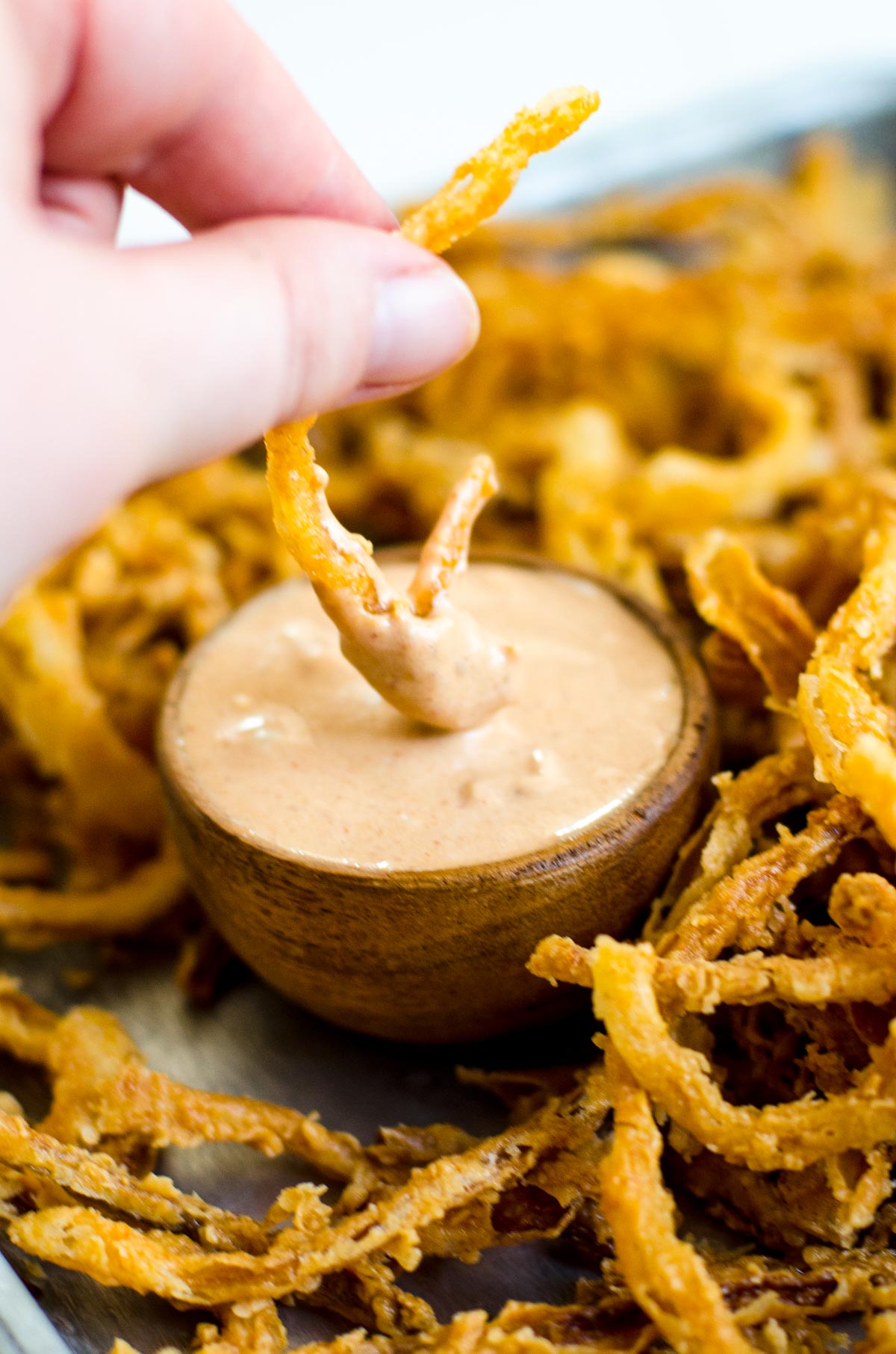 A hand pulling fried onion strings out of dipping sauce.