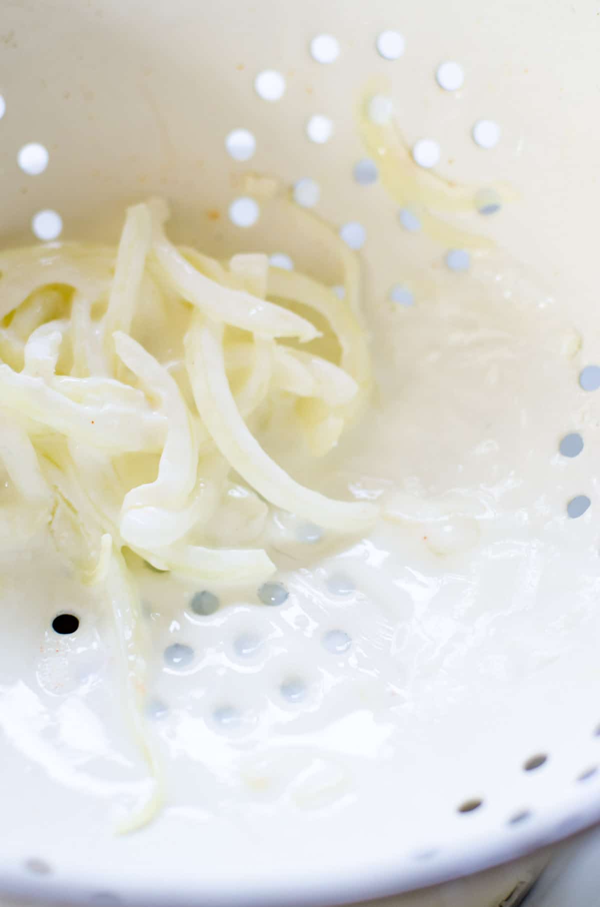 A white colander draining buttermilk from onions.