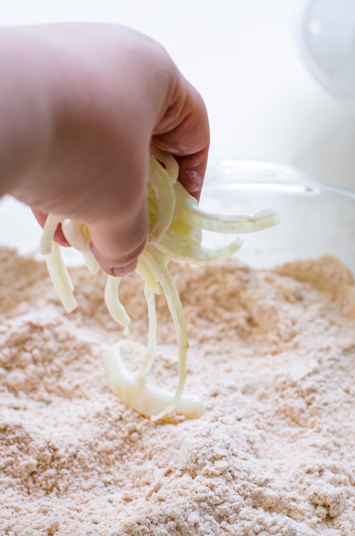 Hand putting onions into flour coating.