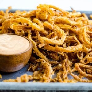 A wooden bowl of sauce next to fried onion strings.