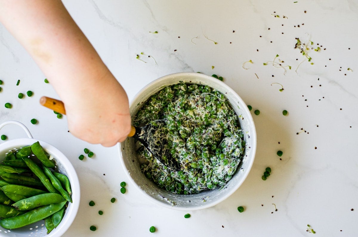 Hands stirring English pea salad together in a bowl.