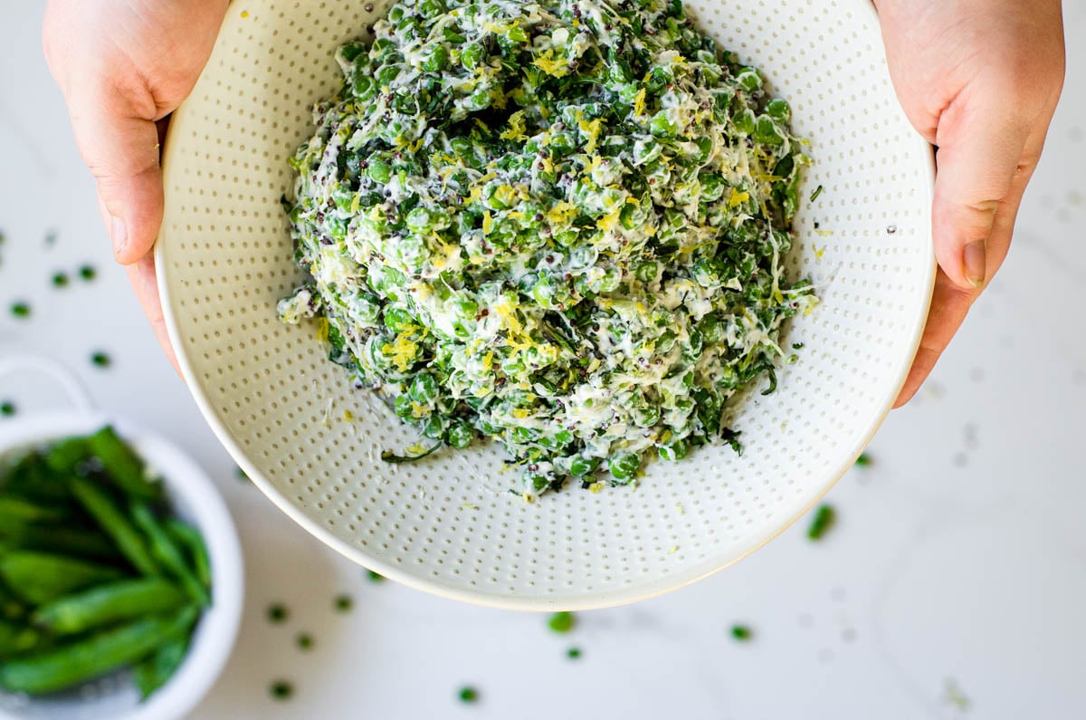 Hands holding a large bowl of English pea salad.