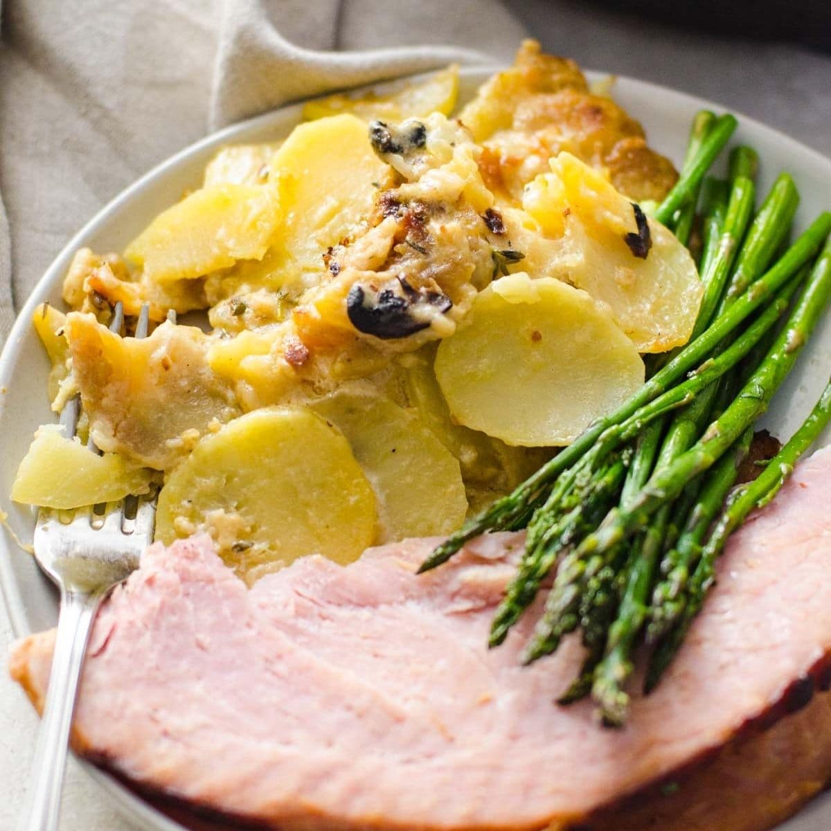 Skillet scalloped potatoes on a plate with asparagus and ham.
