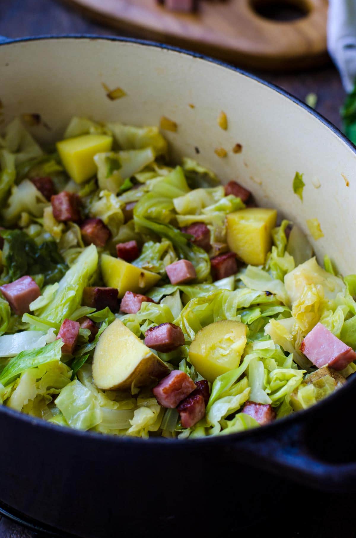 Ham and cabbage with potatoes inside a purple skillet.