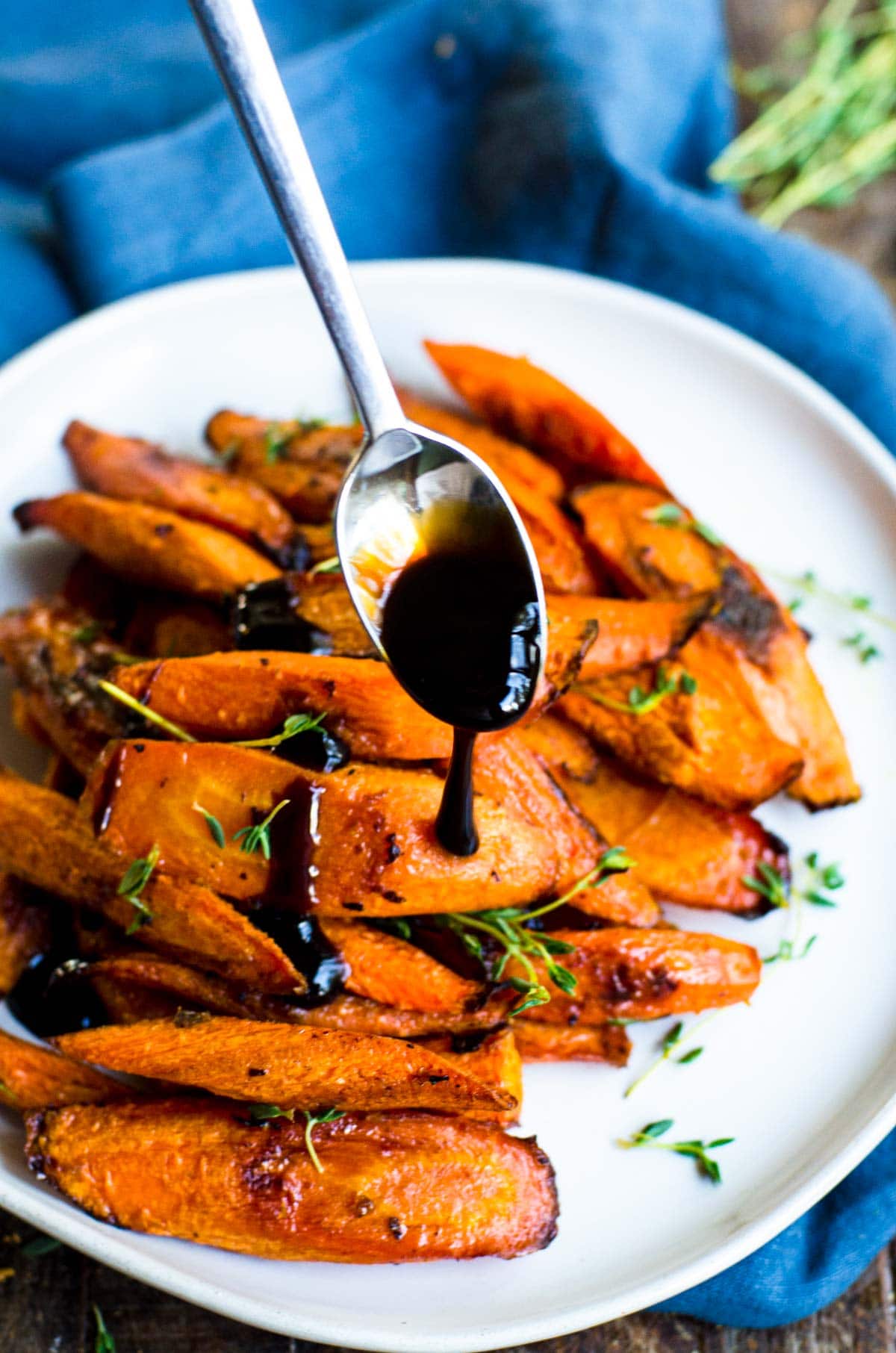 A spoon drizzling balsamic glaze on roasted carrots with thyme.