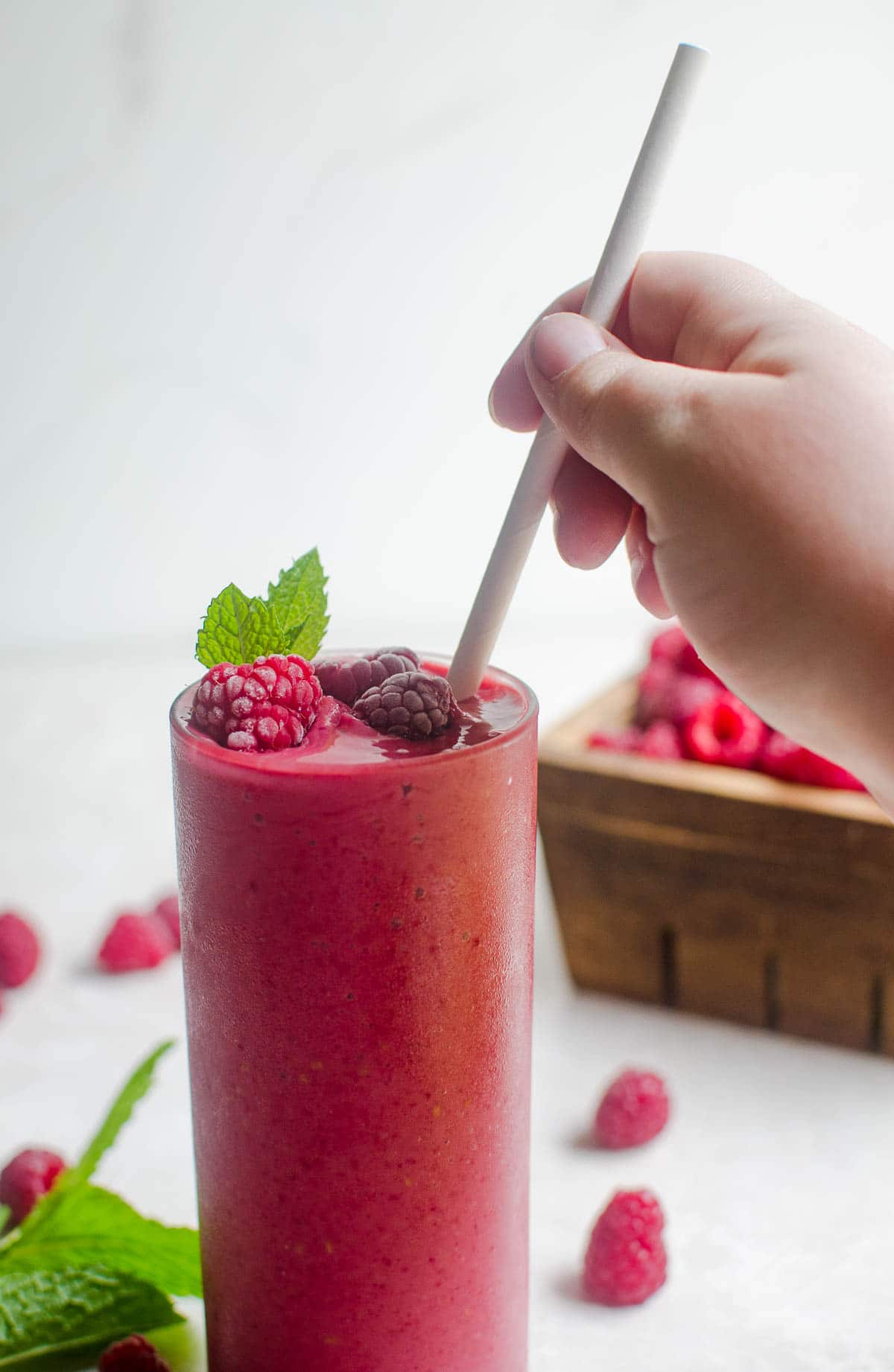 A hand placing a straw into a raspberry smoothie.