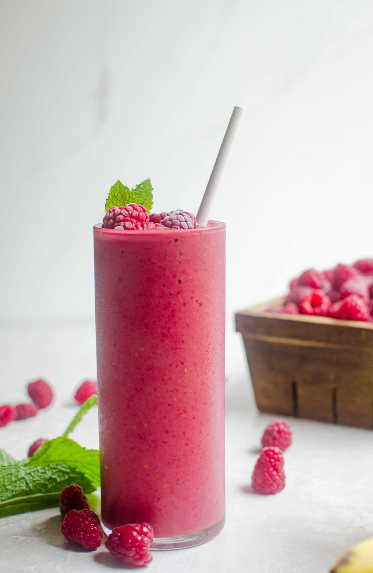 A smoothie on a table surrounded by fresh raspberries and mint.