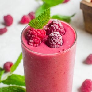 Close up of a glass of raspberry smoothie with frosty berries and mint on top.