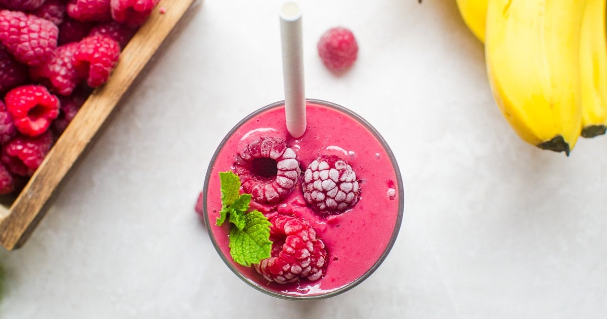 Overhead view of a raspberry smoothie topped with frosty berries, mint, and a straw.