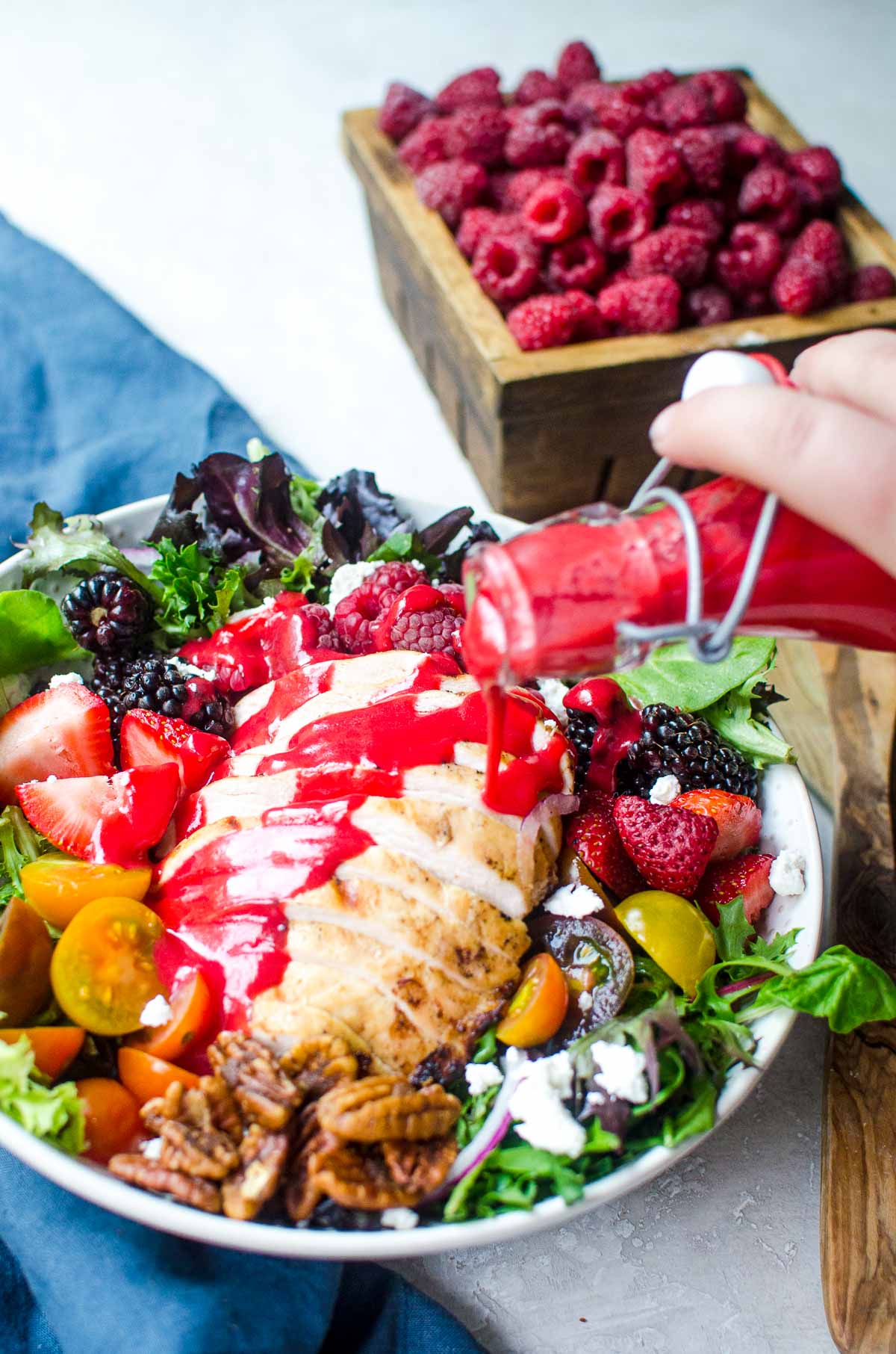 A hand pouring raspberry vinaigrette dressing from bottle onto a salad.