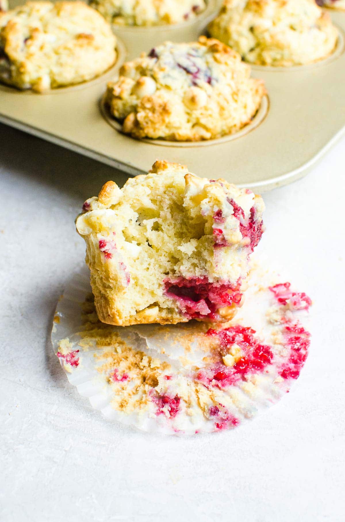 A bite taken out of a raspberry white chocolate muffin showing inside bakery style texture.