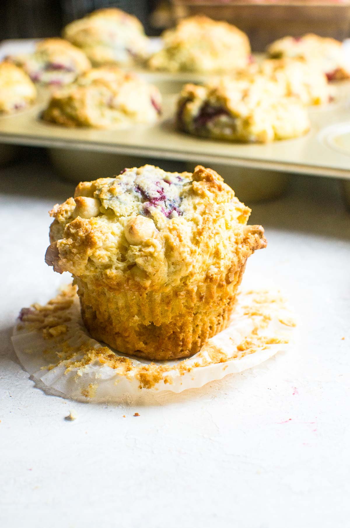 An unwrapped raspberry white chocolate muffin in front of a muffin pan.