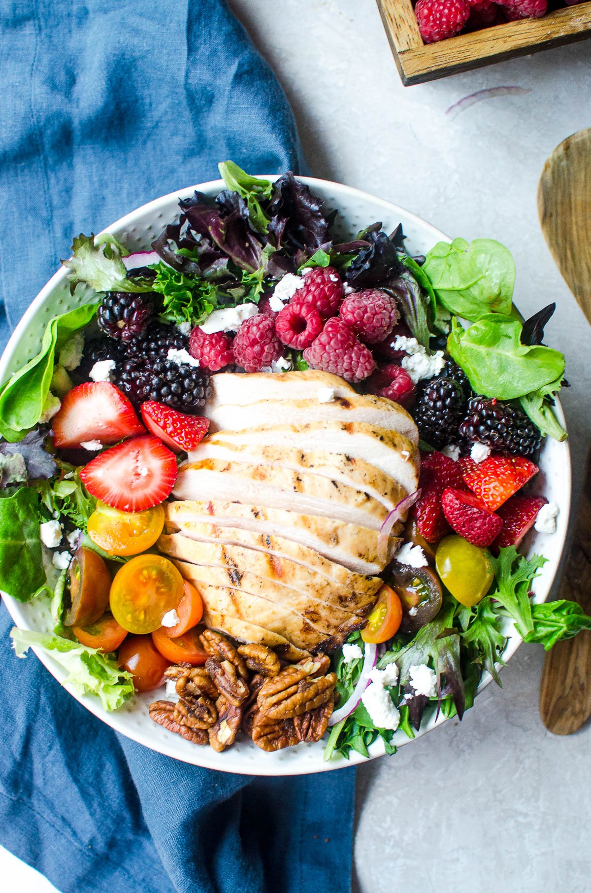 Overhead view of sliced grilled chicken in a bowl with salad greens, berries, and tomatoes.