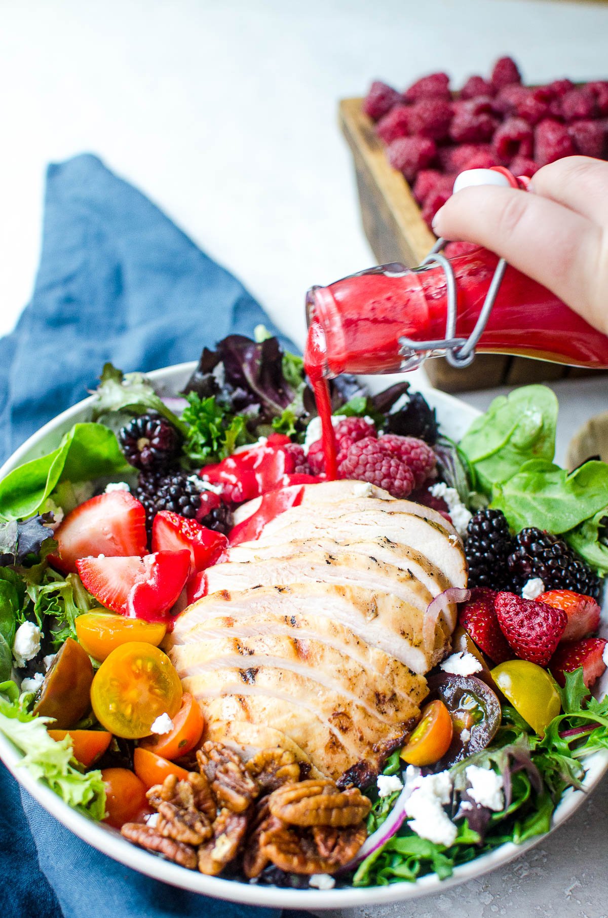 A hand pouring raspberry vinaigrette onto a chicken salad.