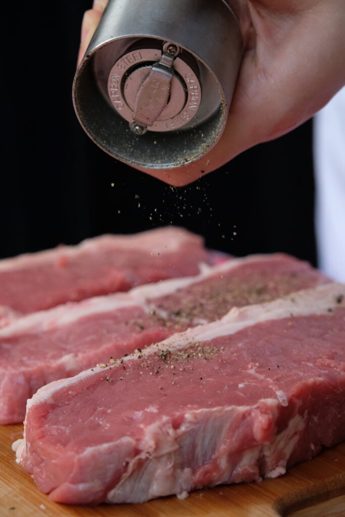 Hand grinding pepper onto raw meat.